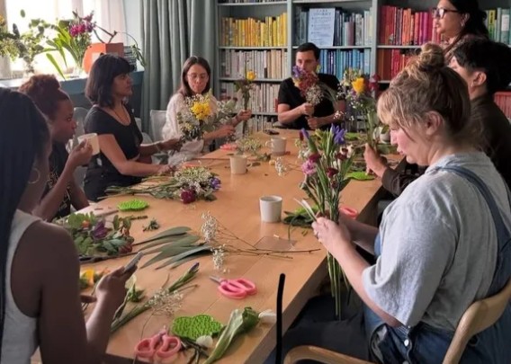A flower therapy workshop around a long table, with guests building bouquets in front of a wall of books