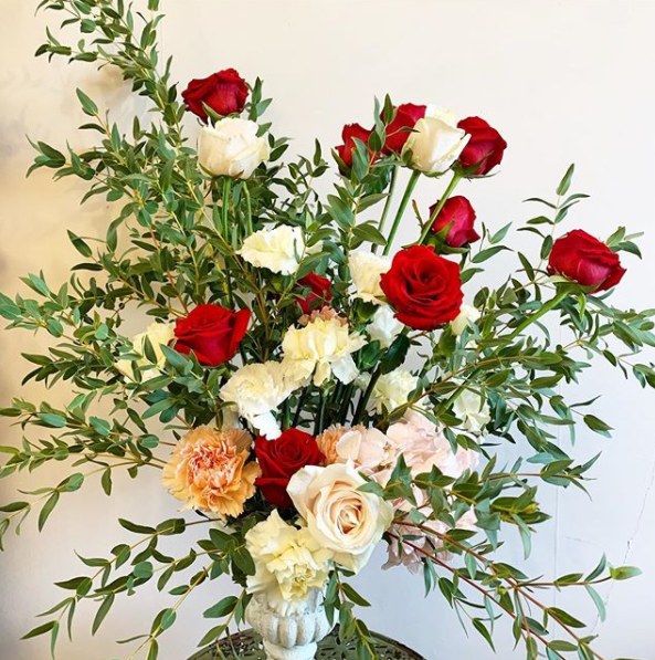 A tall arrangement of red and white roses, carnations and ruscus in a stone urn