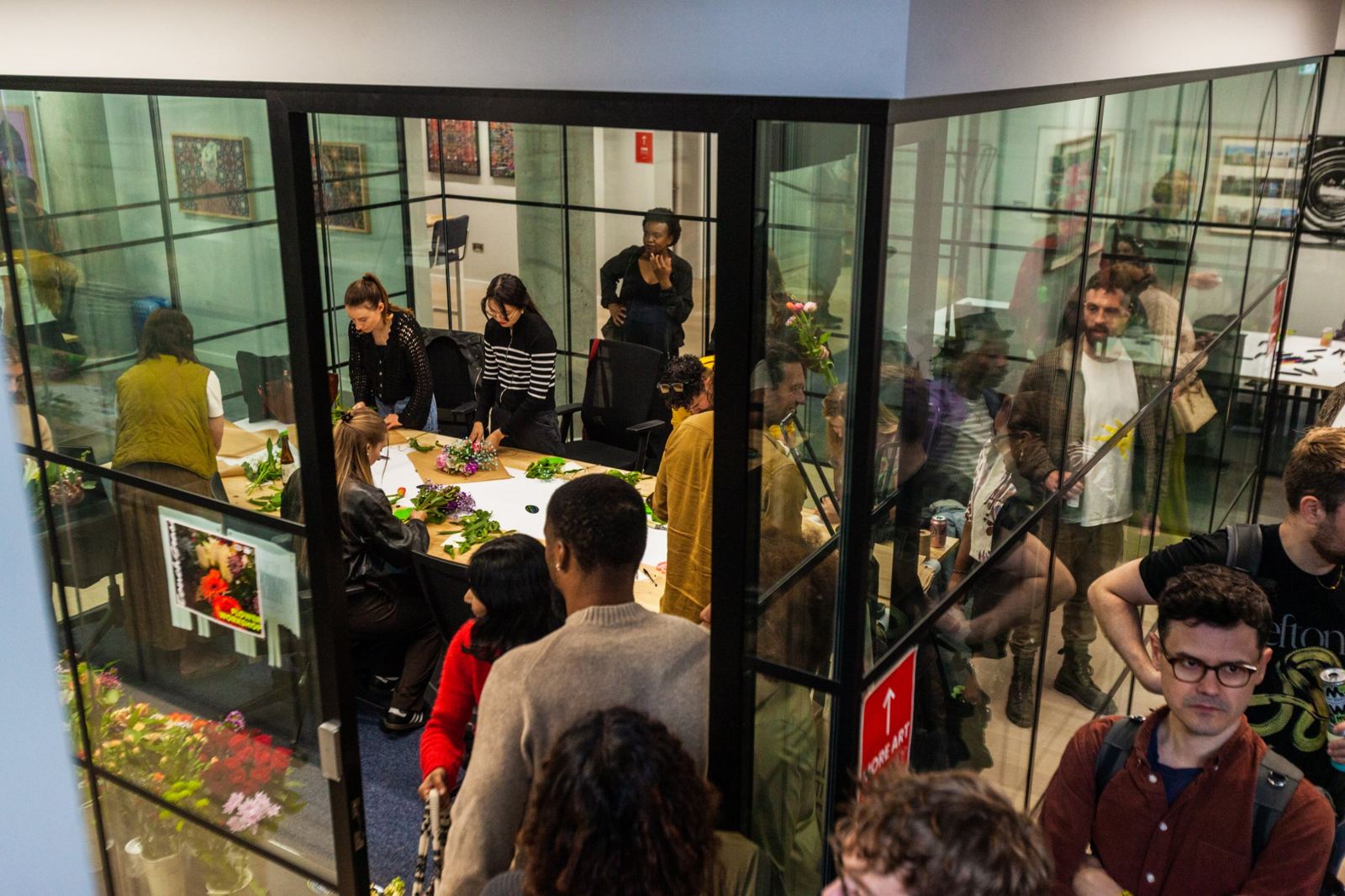 A busy glass-walled room full of people making bouquets